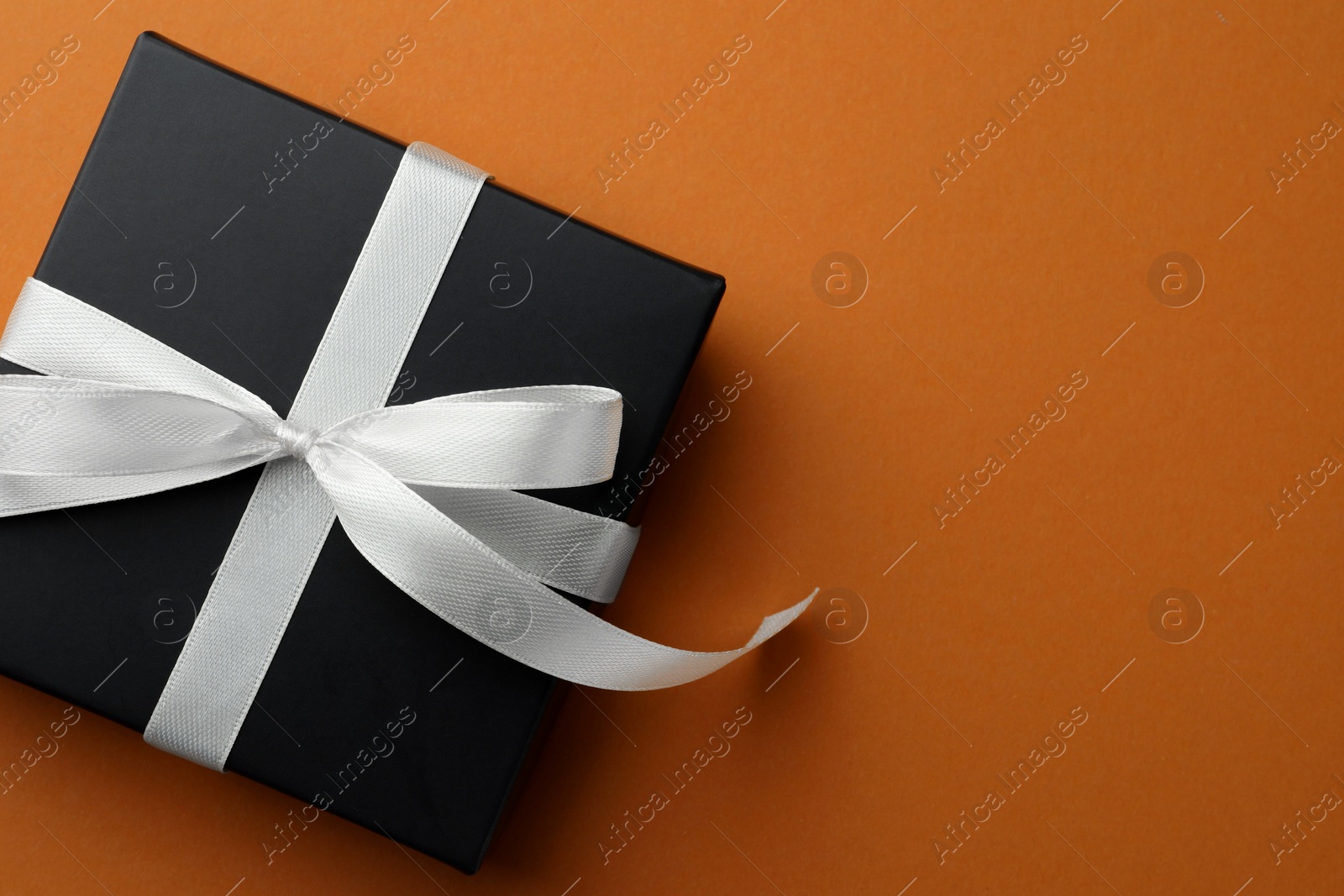 Photo of Beautiful gift box with bow on orange background, top view. Space for text