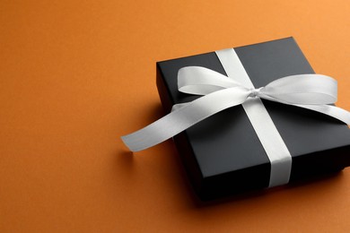 Photo of Beautiful gift box with bow on orange background, closeup. Space for text