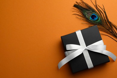 Photo of Beautiful gift box and peacock feather on orange background, top view. Space for text