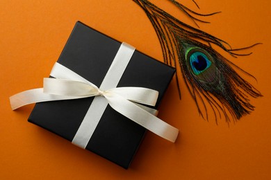 Photo of Beautiful gift box and peacock feather on orange background, top view