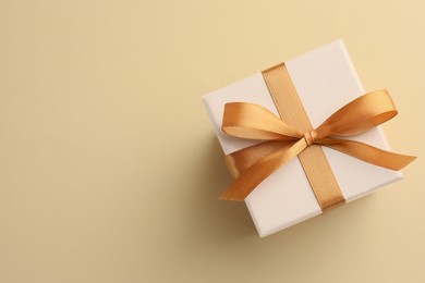 Photo of Beautiful gift box with golden bow on beige background, top view. Space for text