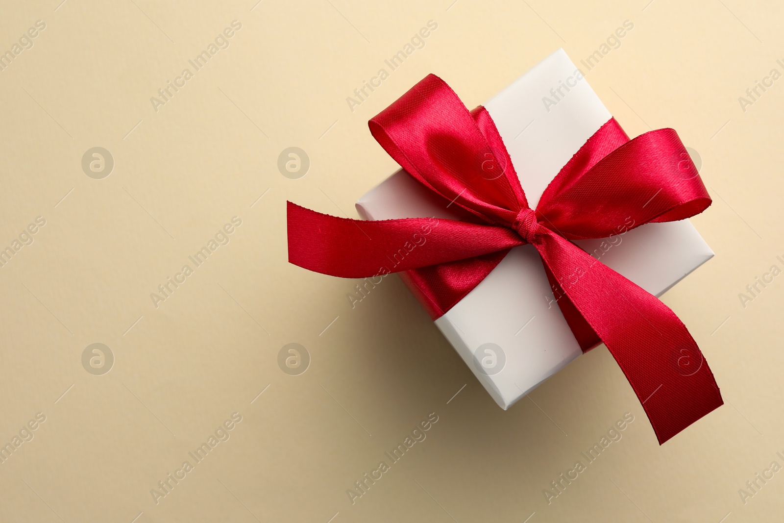 Photo of Beautiful gift box with red bow on beige background, top view. Space for text