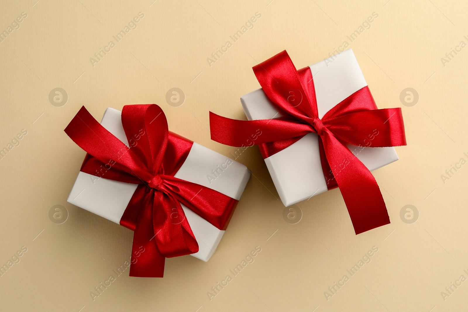 Photo of Beautiful gift boxes with red bows on beige background, top view