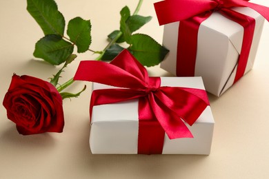 Photo of Beautiful gift boxes with red bows and rose on beige background, closeup