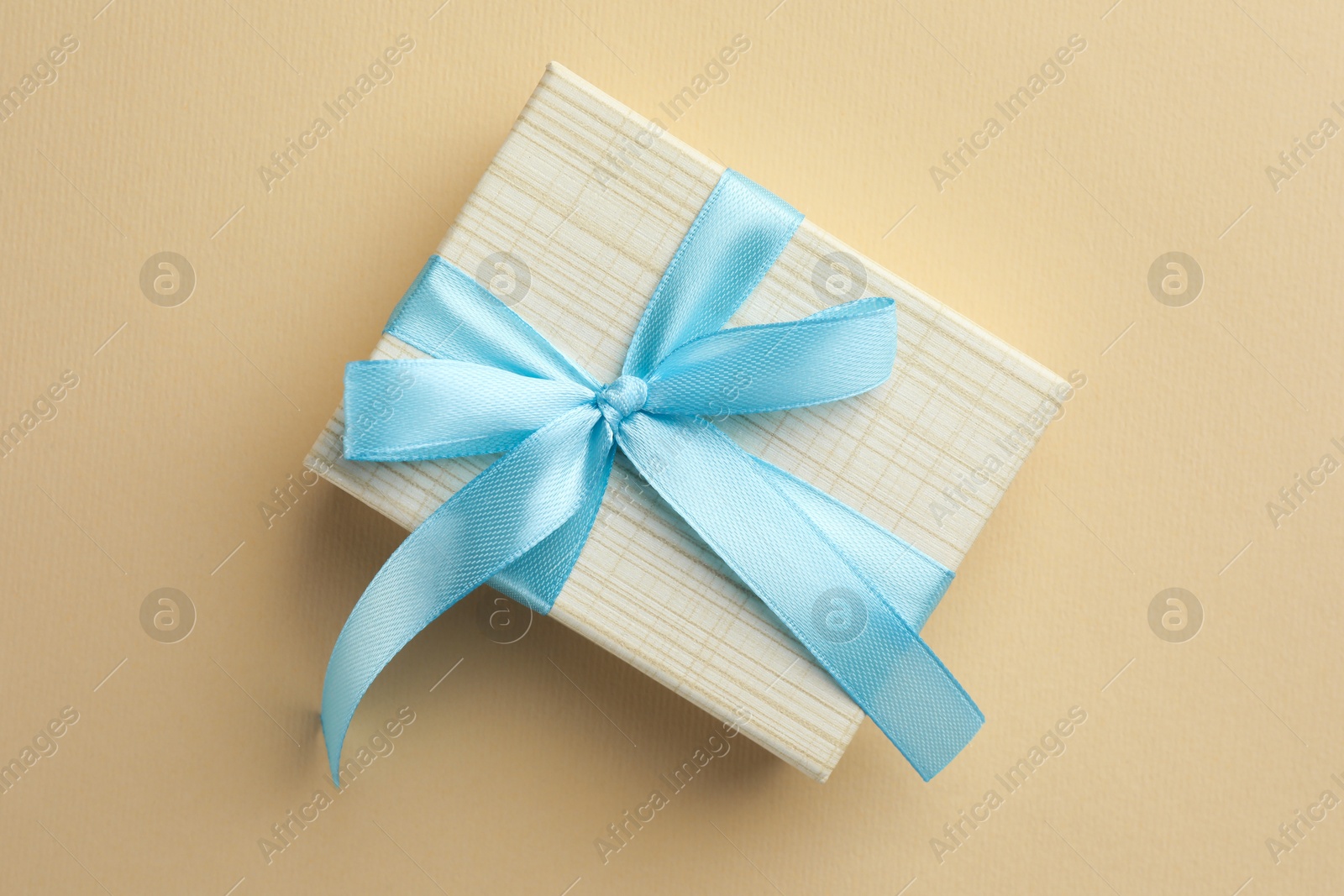 Photo of Beautiful gift box with light blue bow on beige background, top view