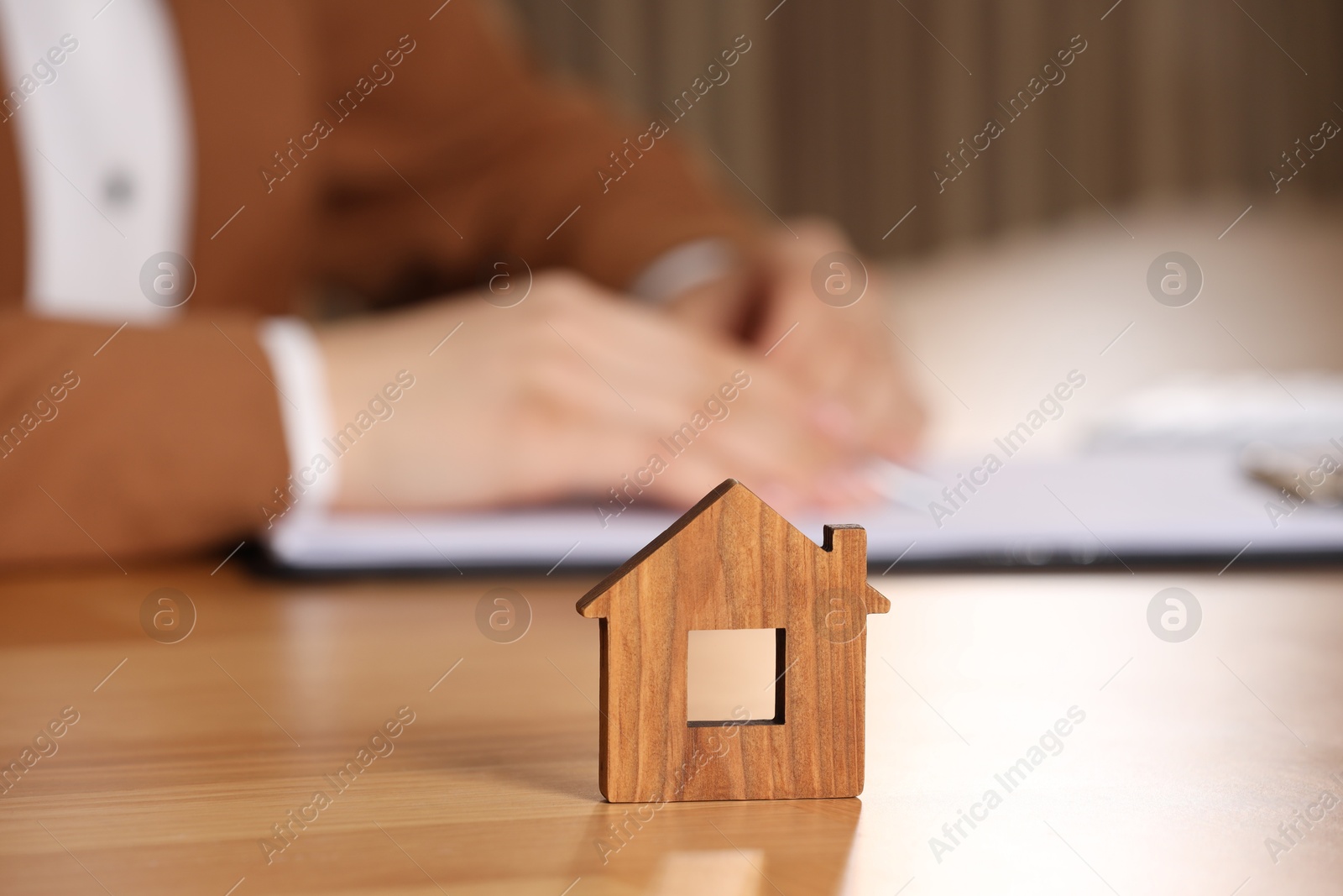 Photo of Property insurance. Real estate agent working at table indoors, focus on wooden house figure