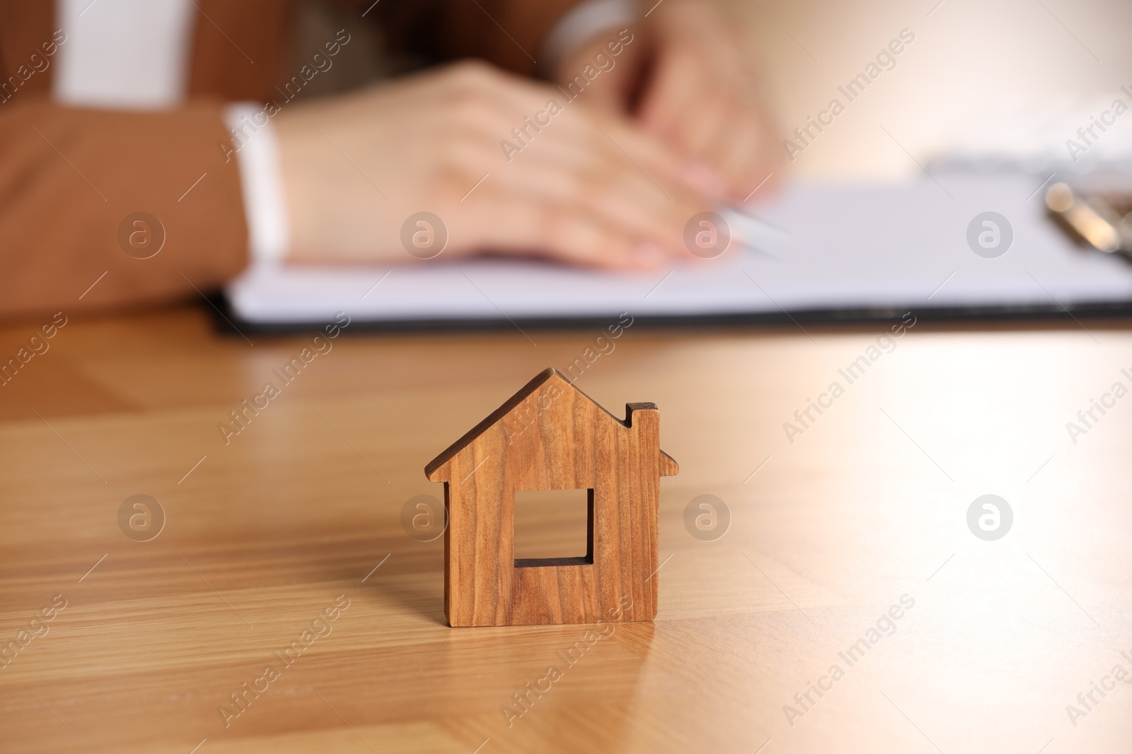 Photo of Property insurance. Real estate agent working at table indoors, focus on wooden house figure