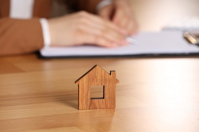 Photo of Property insurance. Real estate agent working at table indoors, focus on wooden house figure