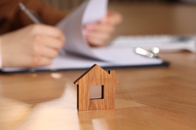 Photo of Property insurance. Real estate agent working at table indoors, focus on wooden house figure