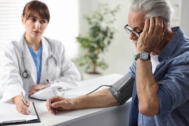 Photo of Doctor measuring senior man's blood pressure and writing results in hospital, selective focus