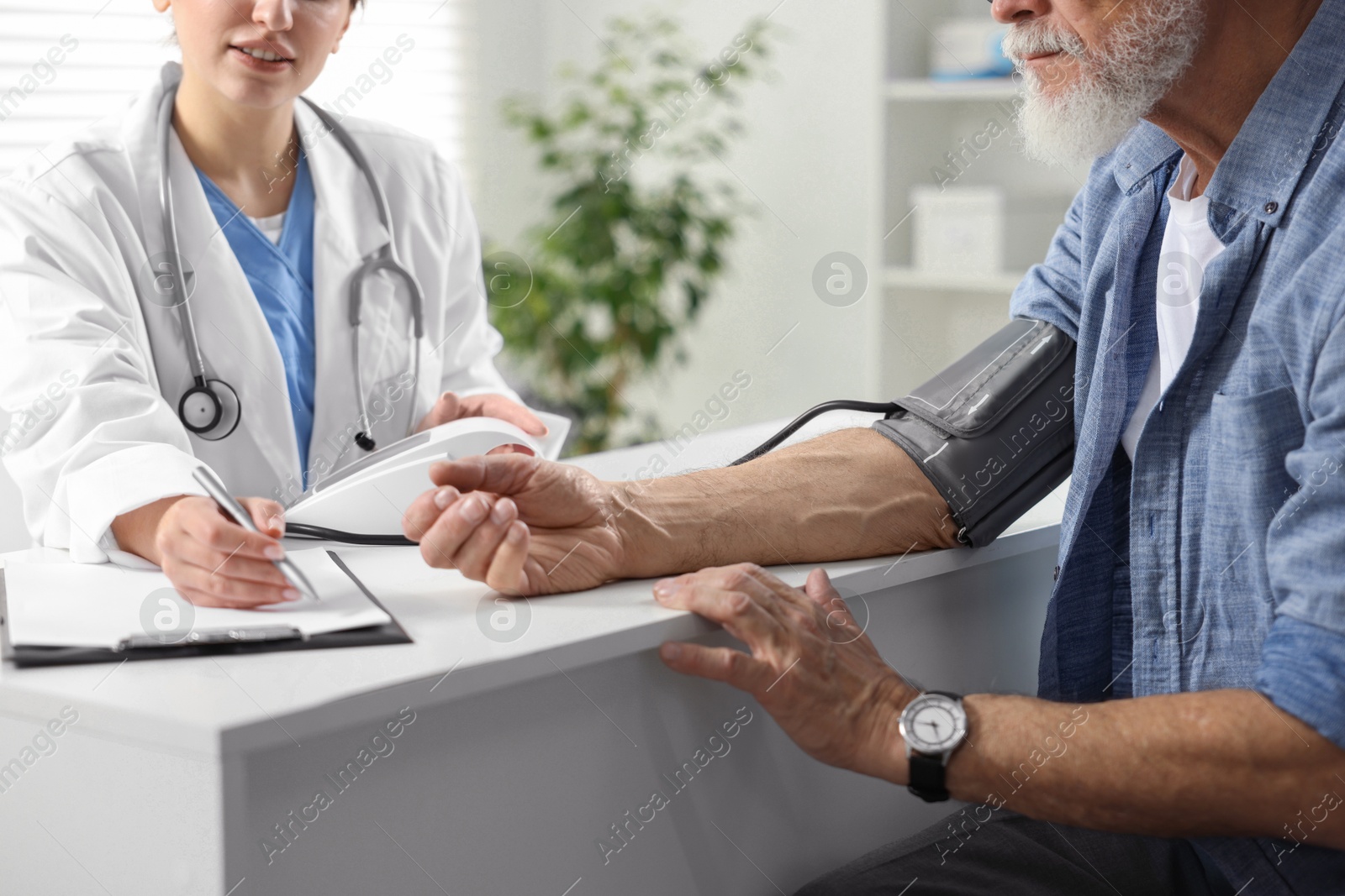 Photo of Doctor measuring senior man's blood pressure and writing results in hospital, closeup