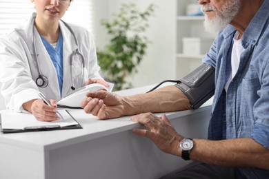 Photo of Doctor measuring senior man's blood pressure and writing results in hospital, closeup