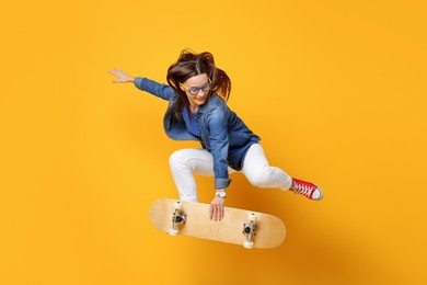 Smiling woman jumping with skateboard on orange background