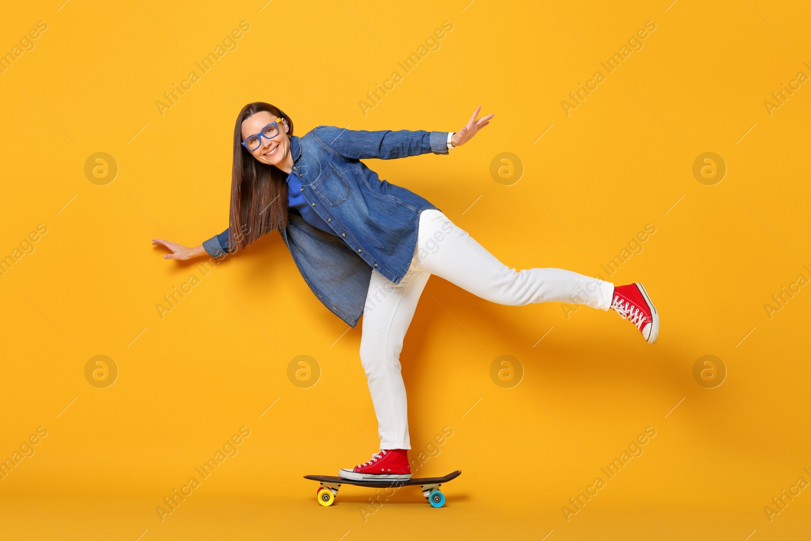 Photo of Smiling woman riding penny board on orange background