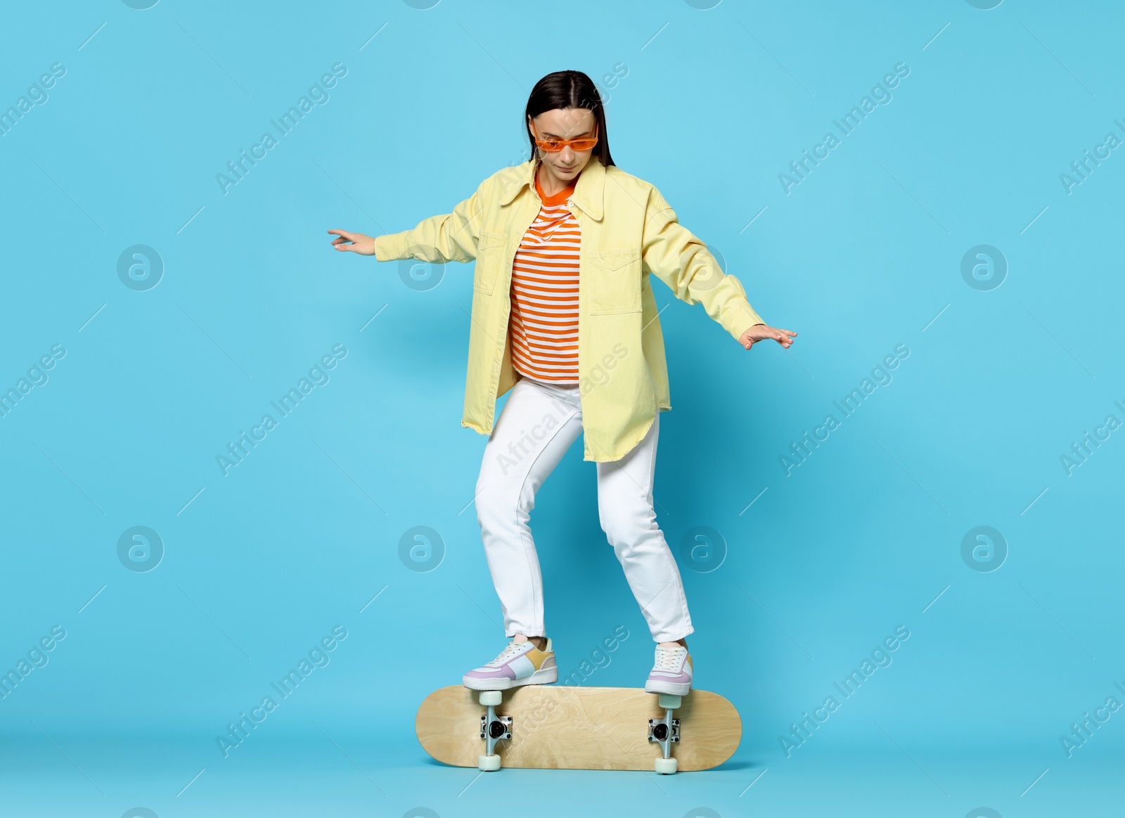 Photo of Beautiful woman on skateboard against light blue background. Space for text