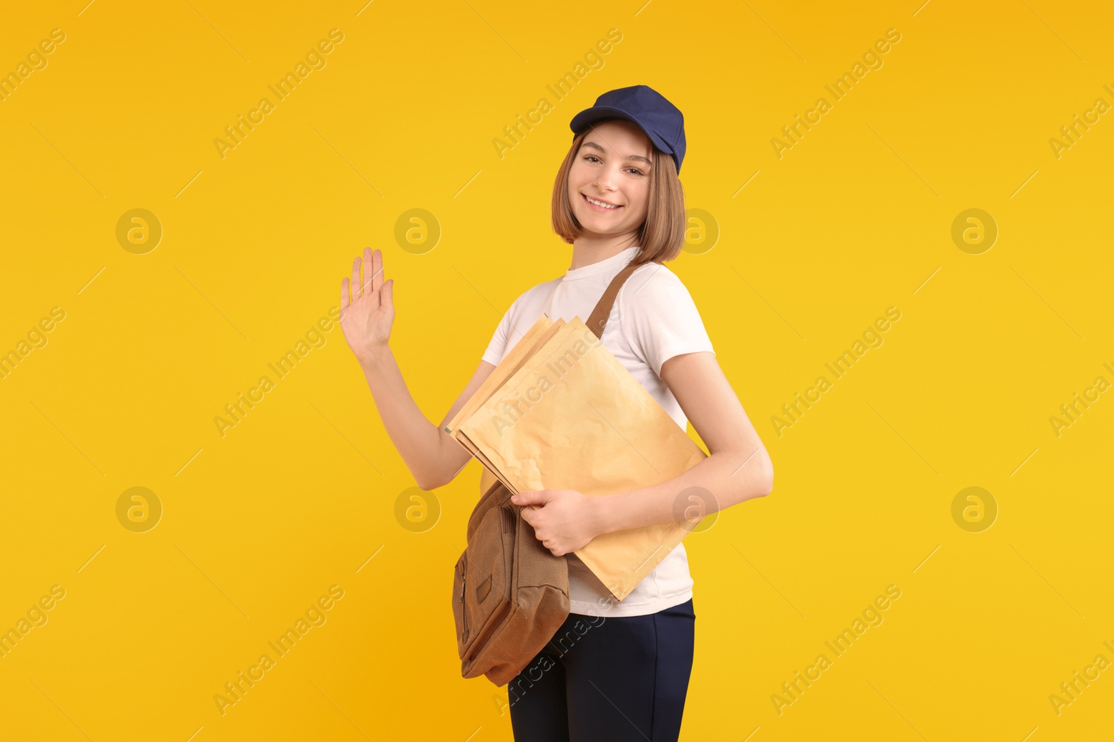 Photo of Happy postwoman with bag and envelopes waving hello on yellow background. Space for text