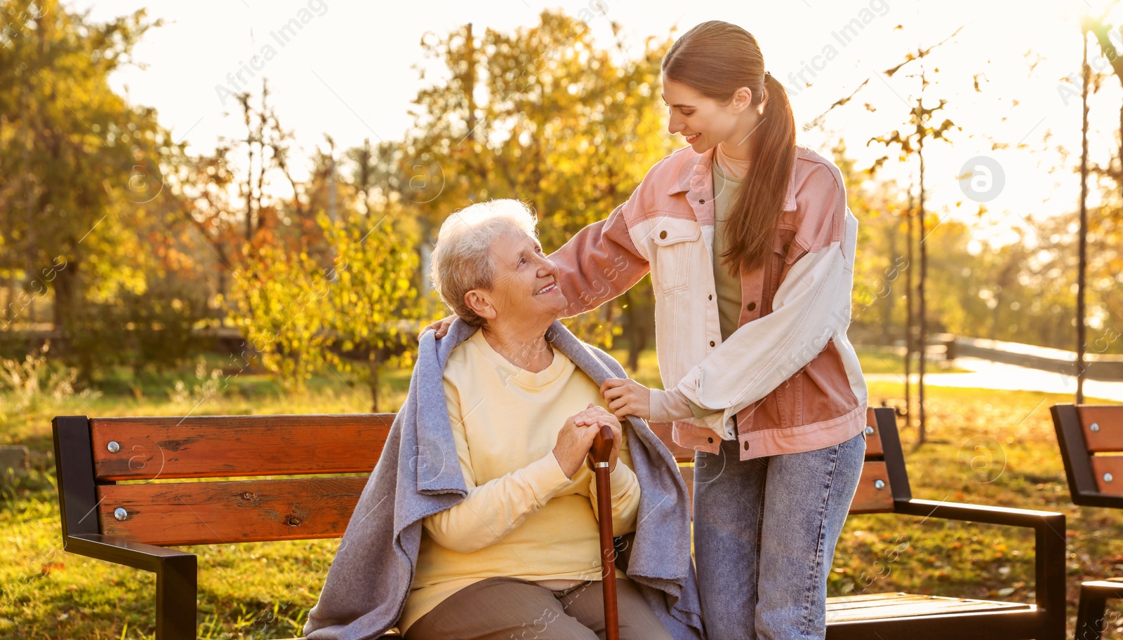 Photo of Elderly woman with walking cane and her caregiver in park