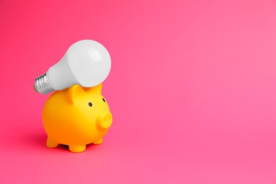 Piggy bank with light bulb on pink background, space for text. Energy saving concept