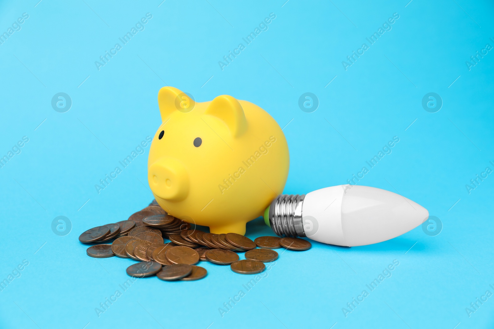 Photo of Piggy bank, coins and lightbulb on light blue background. Energy saving concept