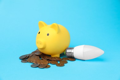 Piggy bank, coins and lightbulb on light blue background. Energy saving concept