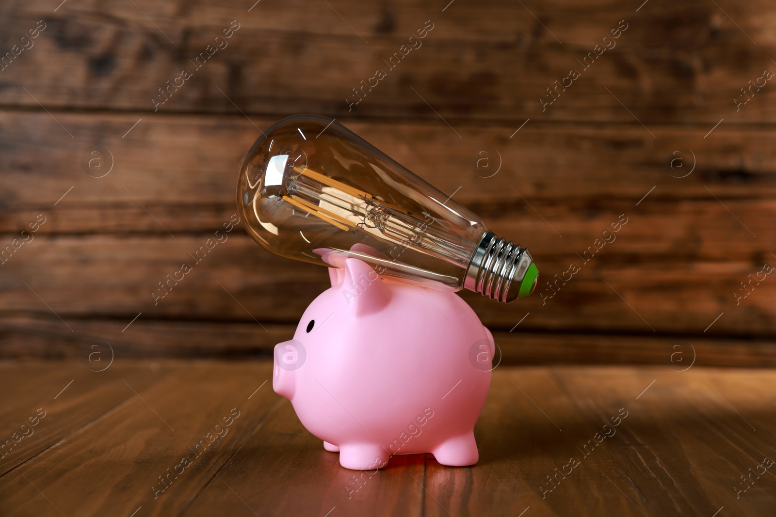 Photo of Piggy bank and light bulb on wooden table. Energy saving concept