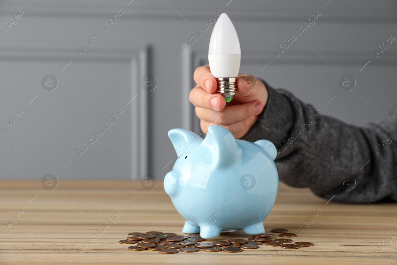 Photo of Energy saving concept. Man holding light bulb above piggy bank at wooden table, closeup. Space for text