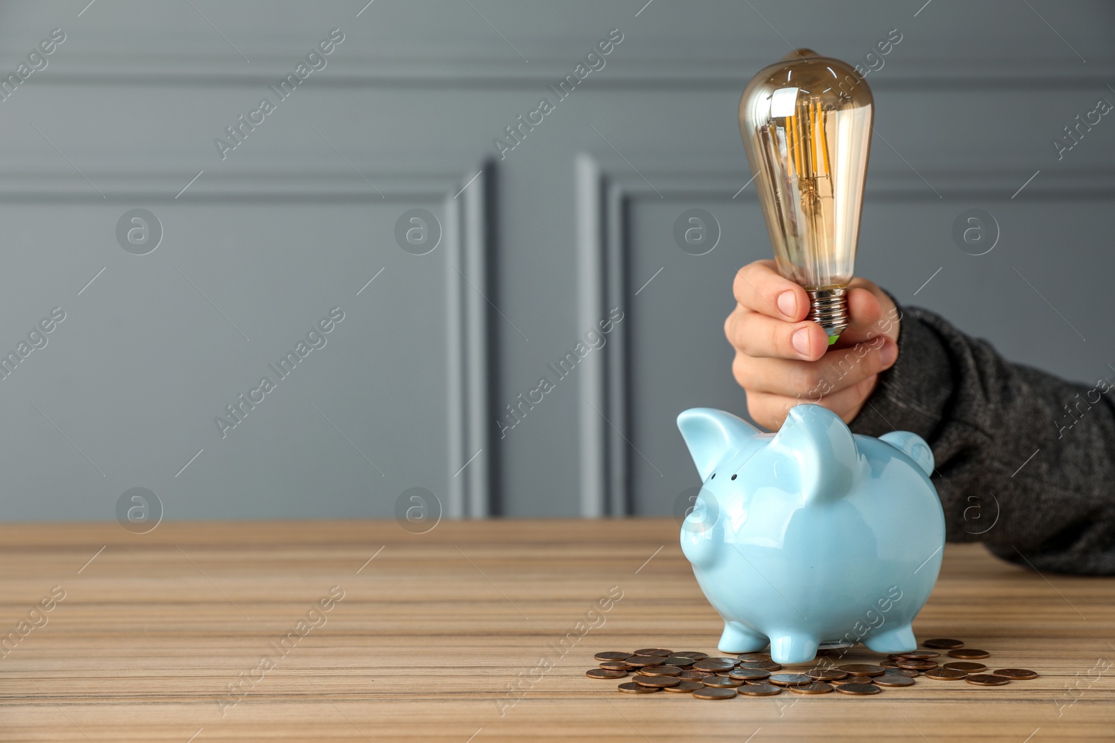 Photo of Energy saving concept. Man holding light bulb above piggy bank at wooden table, closeup. Space for text