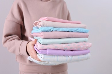 Photo of Woman holding stack of clean bed linens on light background, closeup