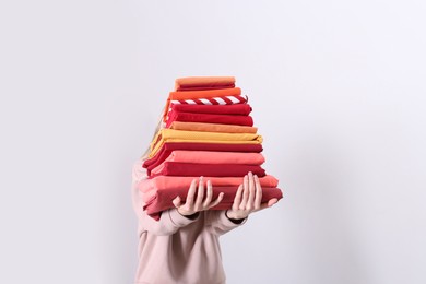 Woman holding stack of clean bed linens on light background