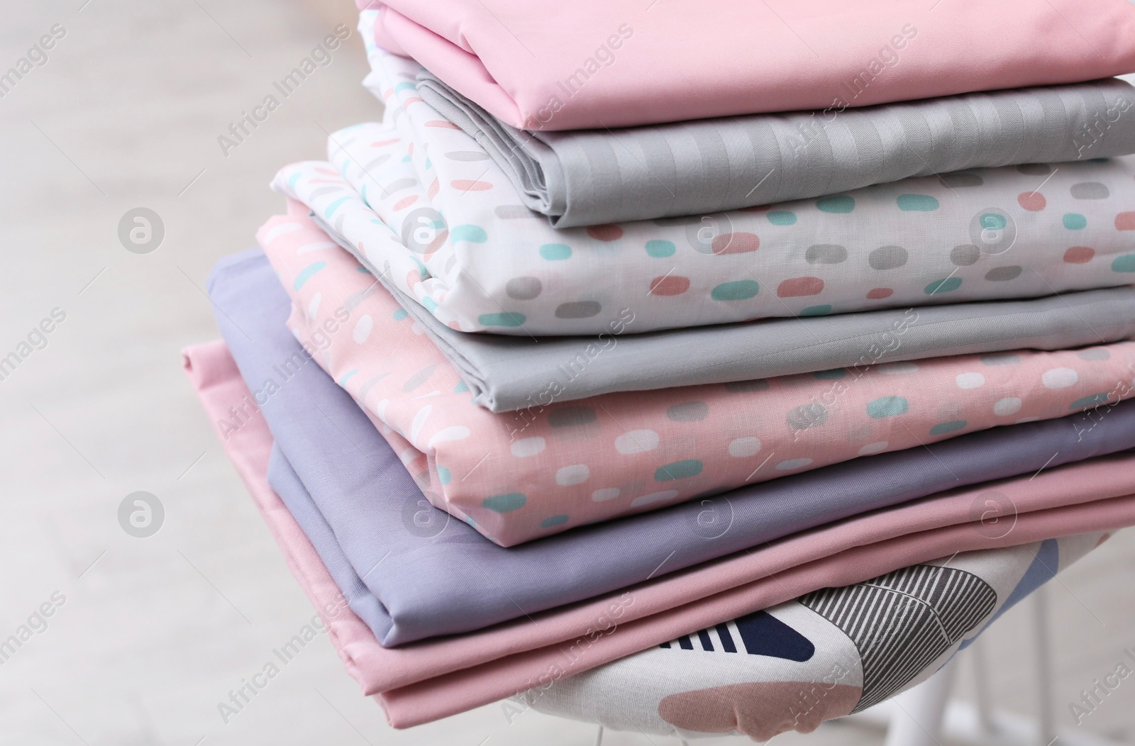 Photo of Stack of clean bed linens on ironing board in room