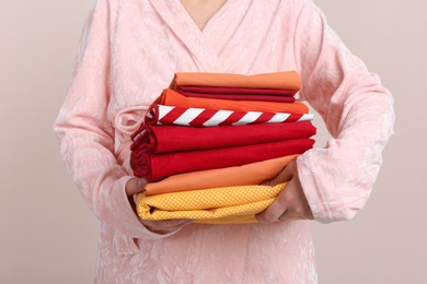 Woman holding stack of clean bed linens on beige background, closeup