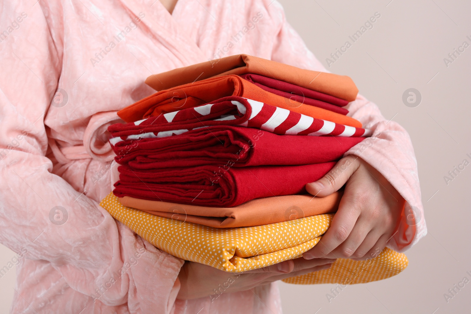 Photo of Woman holding stack of clean bed linens on beige background, closeup