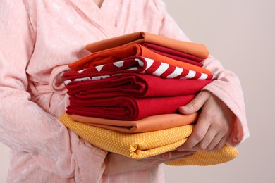 Photo of Woman holding stack of clean bed linens on beige background, closeup