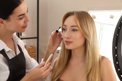 Professional makeup artist working with beautiful young woman in salon. Using ring lamp