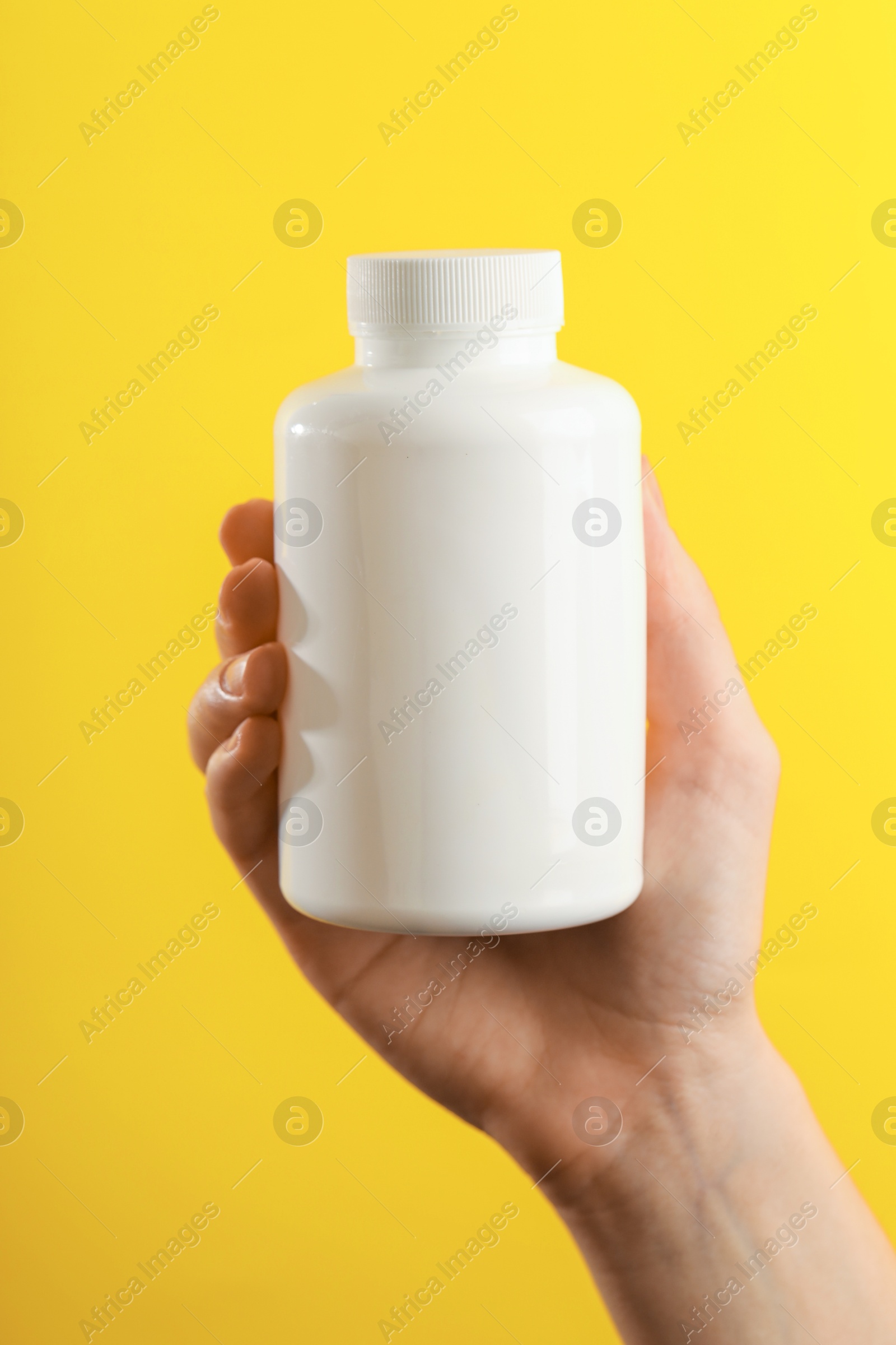 Photo of Woman holding medical bottle with pills on yellow background, closeup