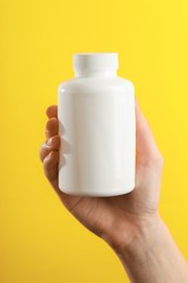 Photo of Woman holding medical bottle with pills on yellow background, closeup