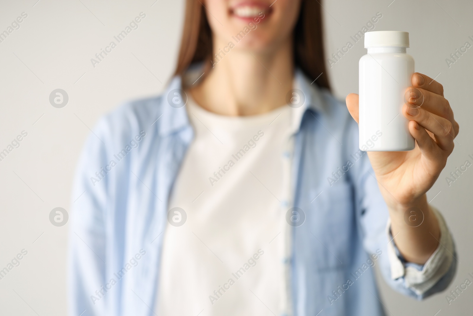 Photo of Woman holding medical bottle with pills on light background, closeup