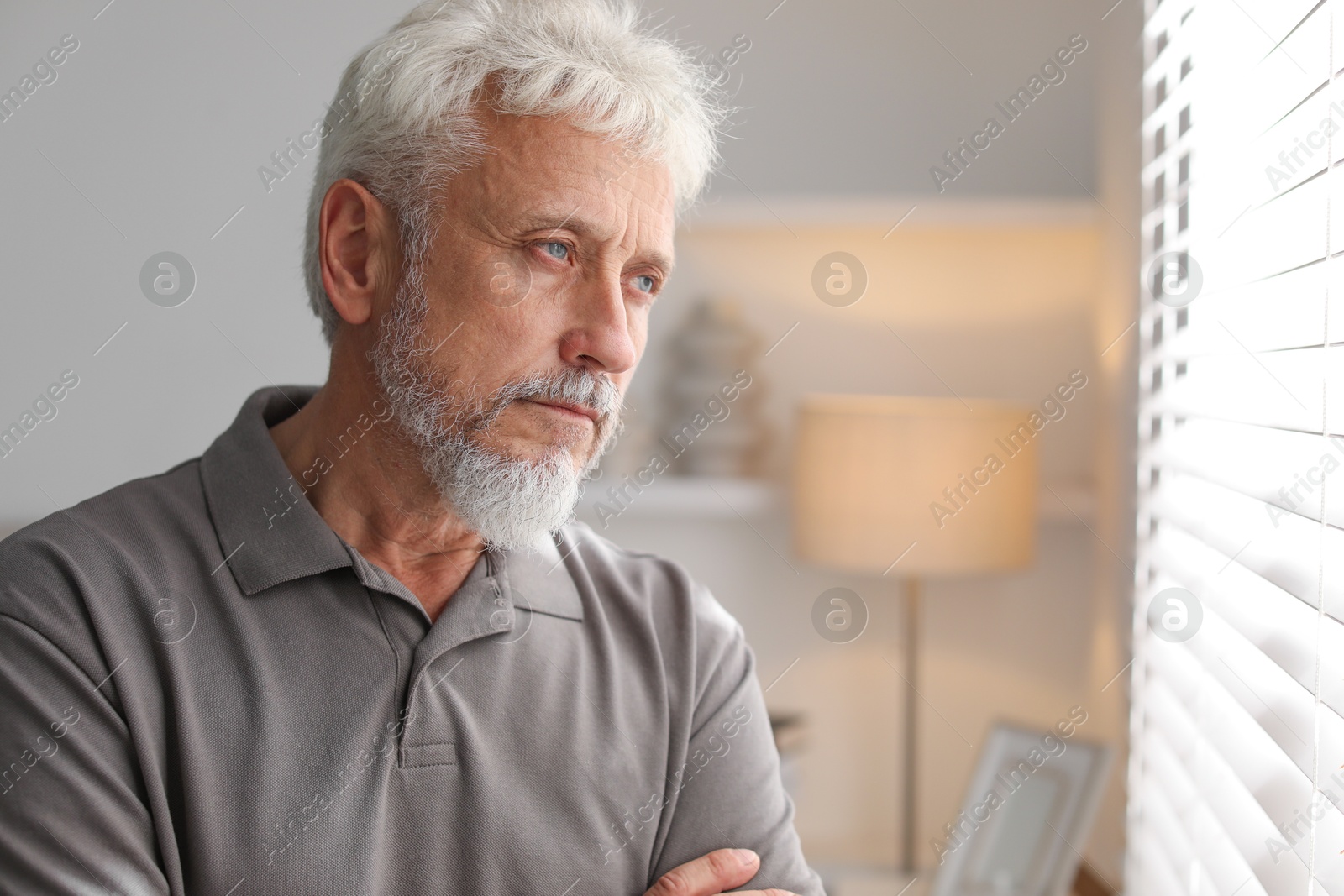 Photo of Lonely senior man looking out window indoors. Space for text