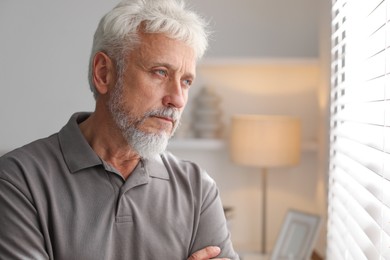 Photo of Lonely senior man looking out window indoors. Space for text