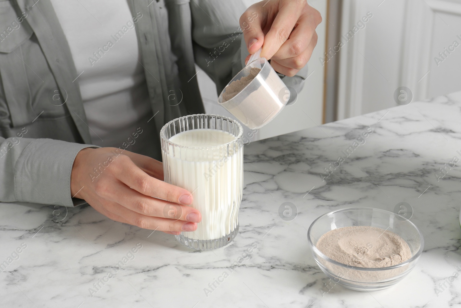 Photo of Making protein cocktail. Woman adding powder into glass with milk at white marble table, closeup