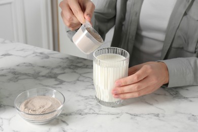 Photo of Making protein cocktail. Woman adding powder into glass with milk at white marble table, closeup