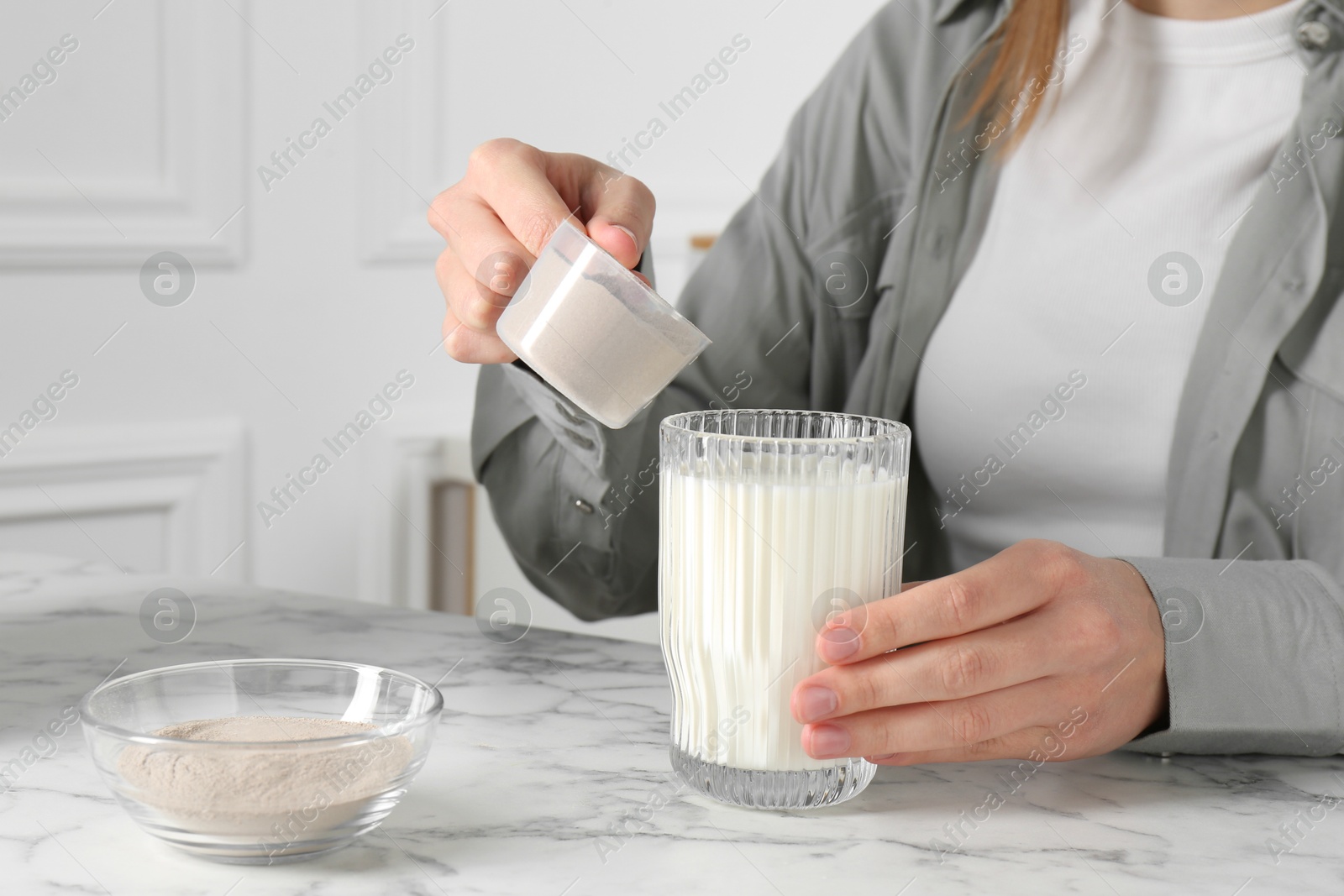 Photo of Making protein cocktail. Woman adding powder into glass with milk at white marble table, closeup