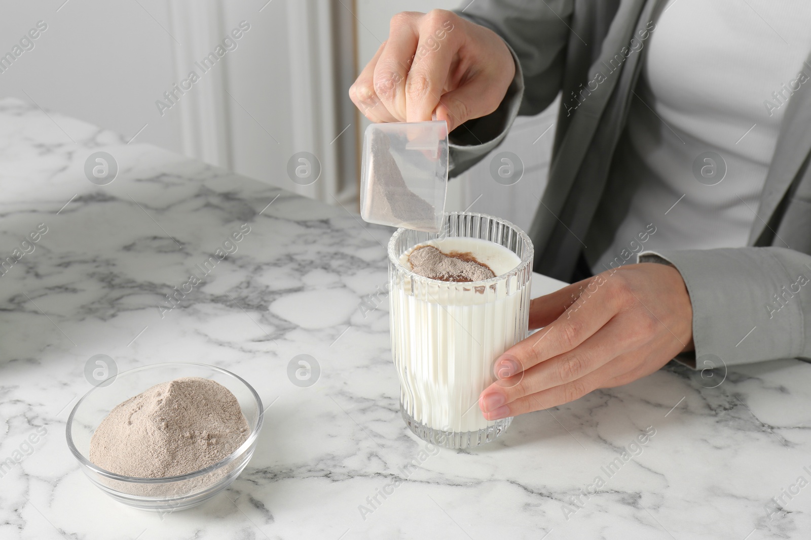 Photo of Making protein cocktail. Woman adding powder into glass with milk at white marble table, closeup