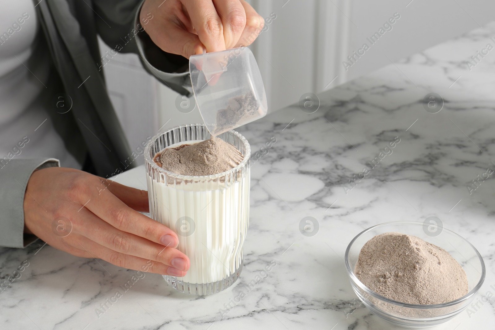 Photo of Making protein cocktail. Woman adding powder into glass with milk at white marble table, closeup