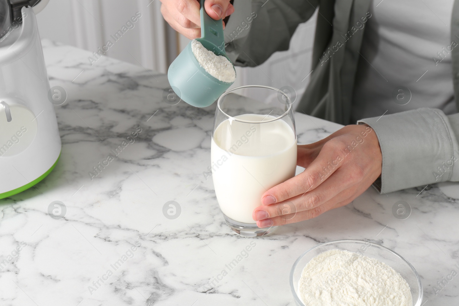 Photo of Making protein cocktail. Woman adding powder into glass with milk at white marble table, closeup