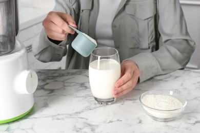 Photo of Making protein cocktail. Woman adding powder into glass with milk at white marble table, closeup