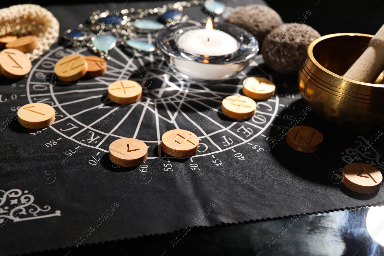 Photo of Wooden runes and burning candle on divination mat, closeup