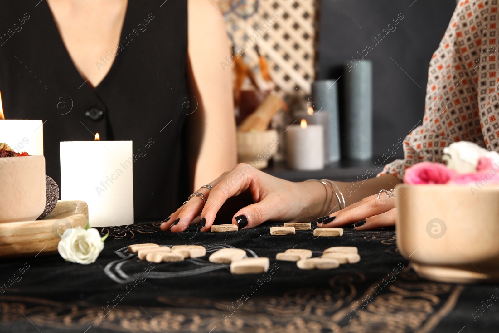 Photo of Fortuneteller with wooden runes reading woman's future at divination mat, closeup