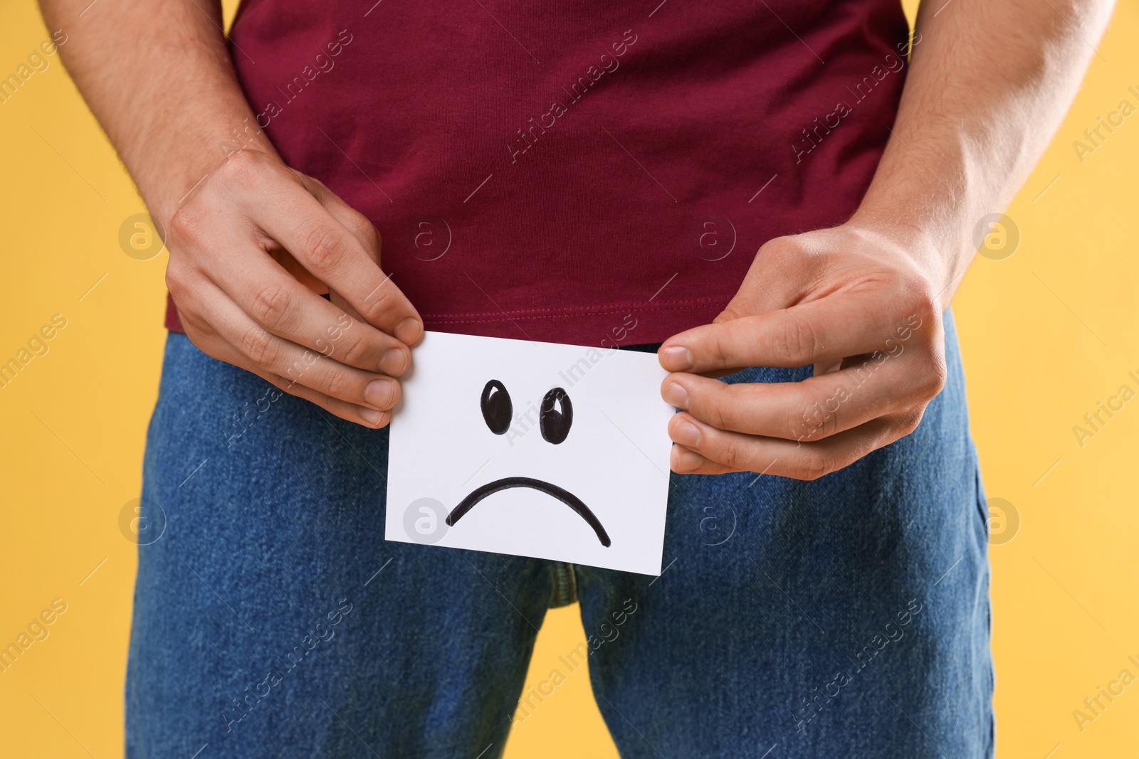 Photo of STD (sexually transmitted diseases). Man holding sticky note with drawn sad face on yellow background, closeup