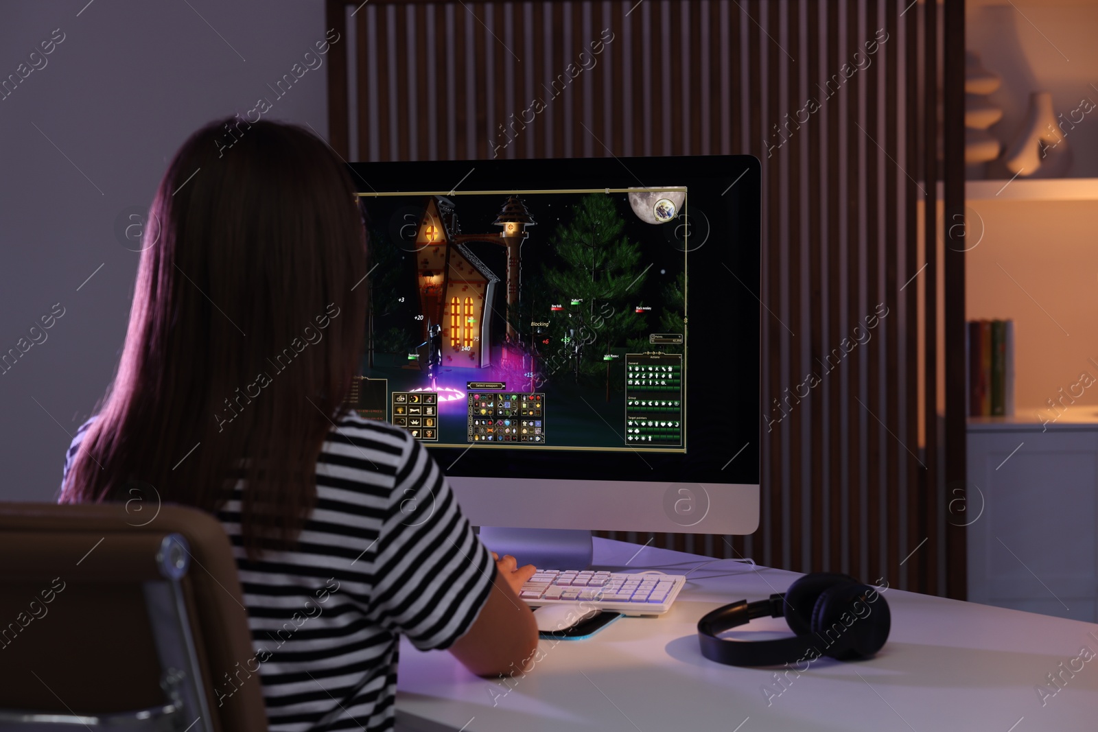 Photo of Woman playing video game with keyboard at table indoors, back view